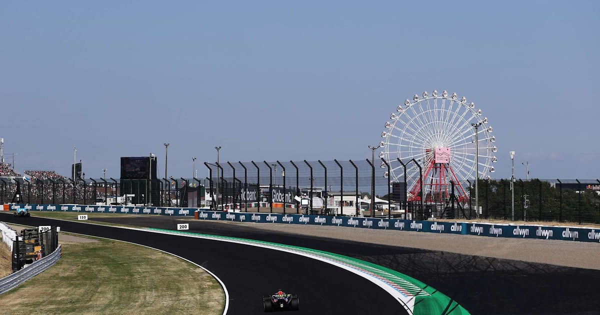 A Red Bull Formula 1 car passes through Suzuka with the circuit ferris wheel rising above the track.